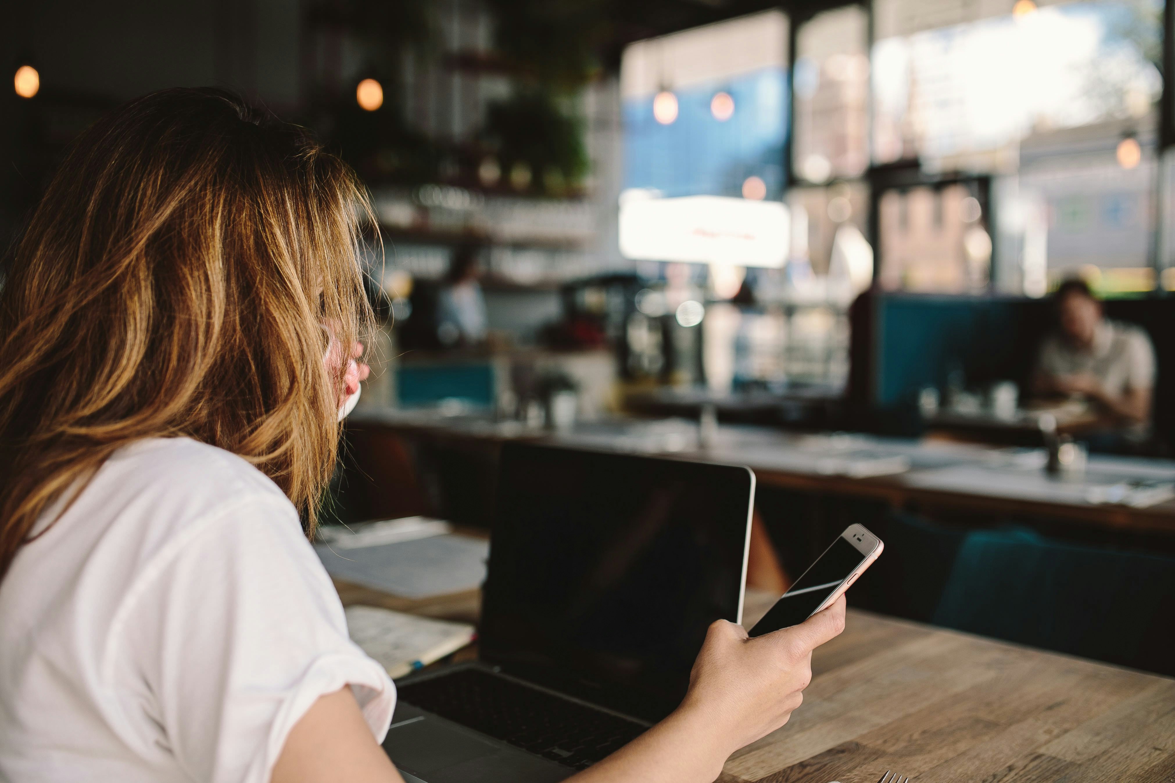 a woman with a laptop and phone at a cafe table