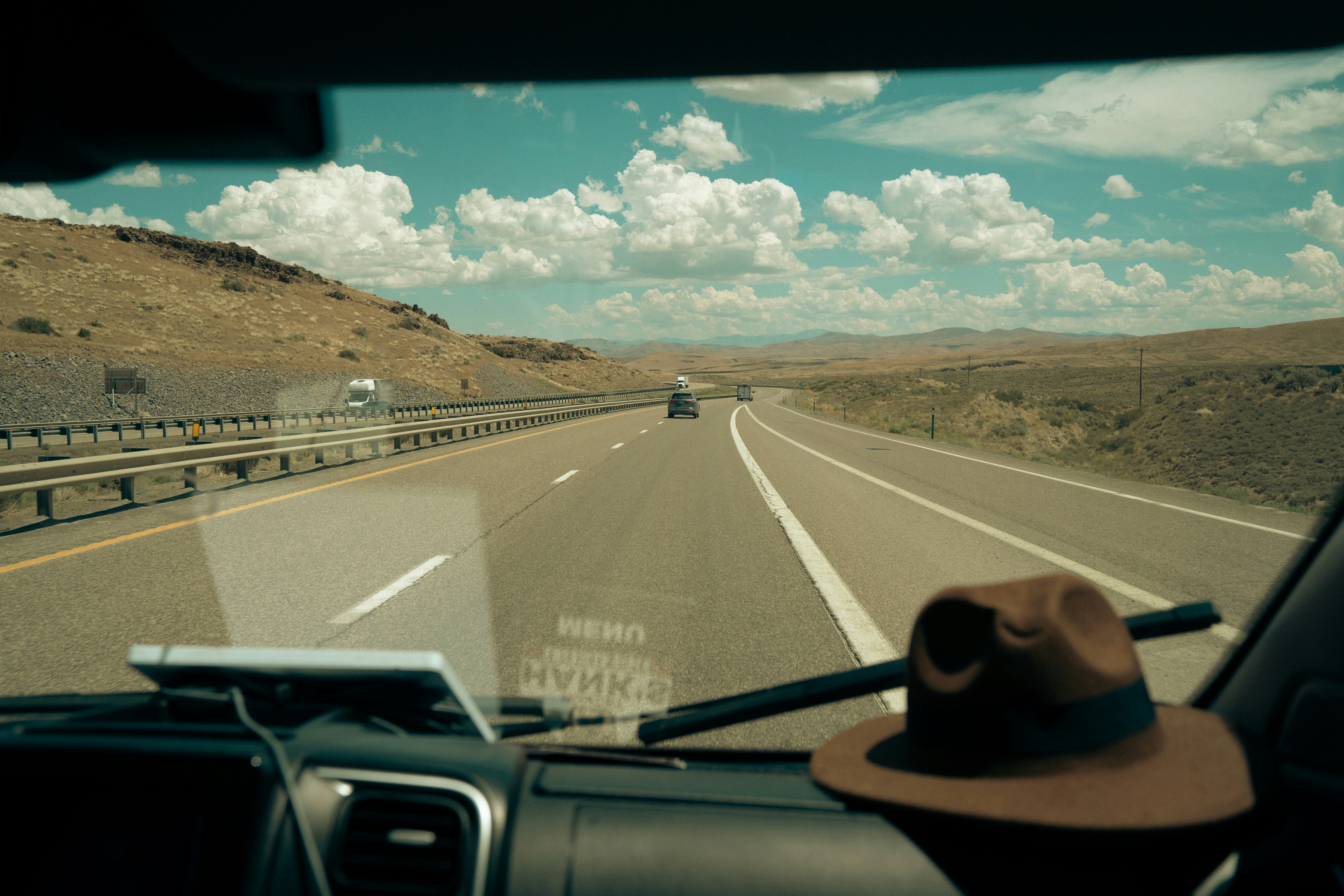 an open road seen from the passenger seat with a hat on the dash