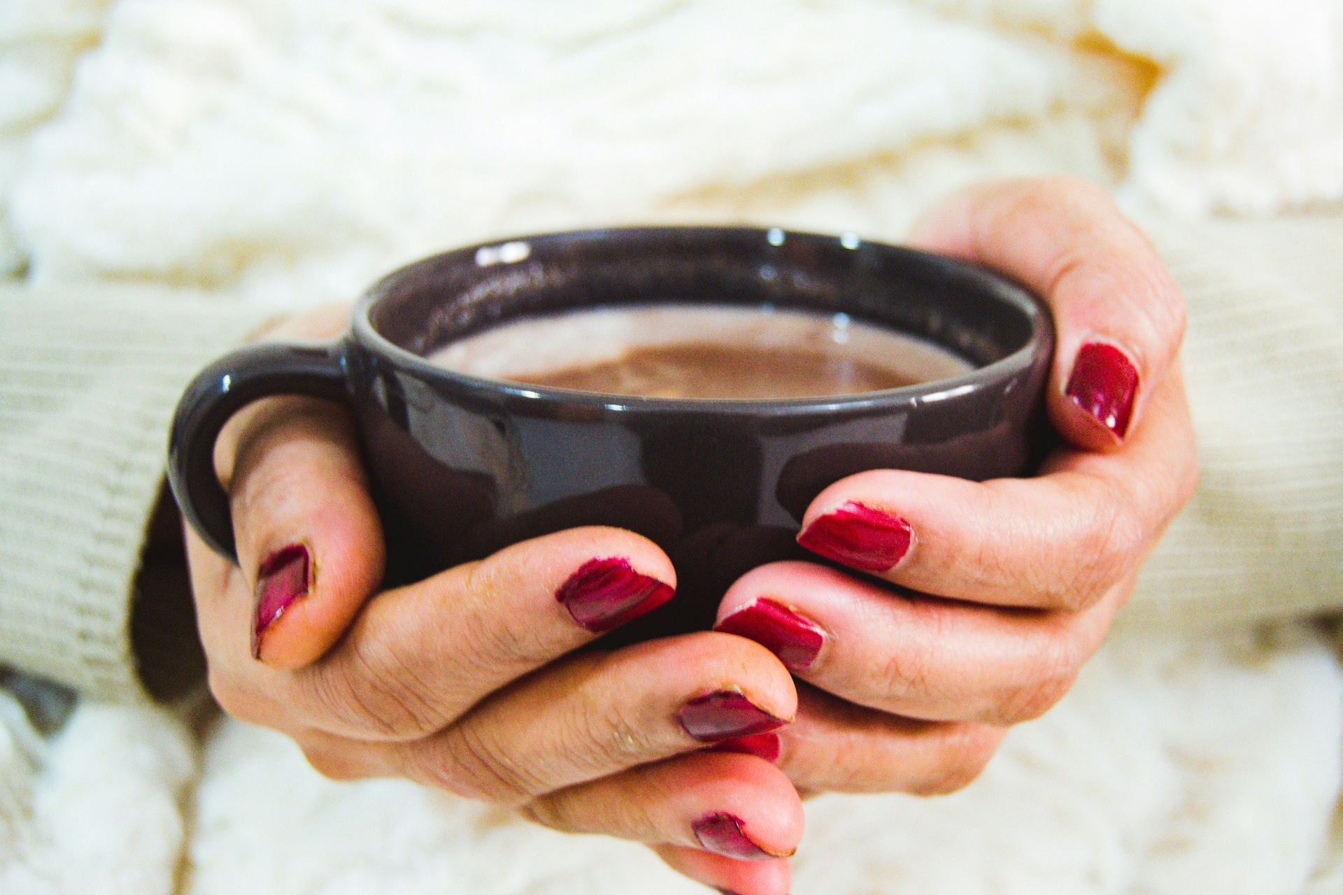 hands warming around a dark mug over a knitted blanket
