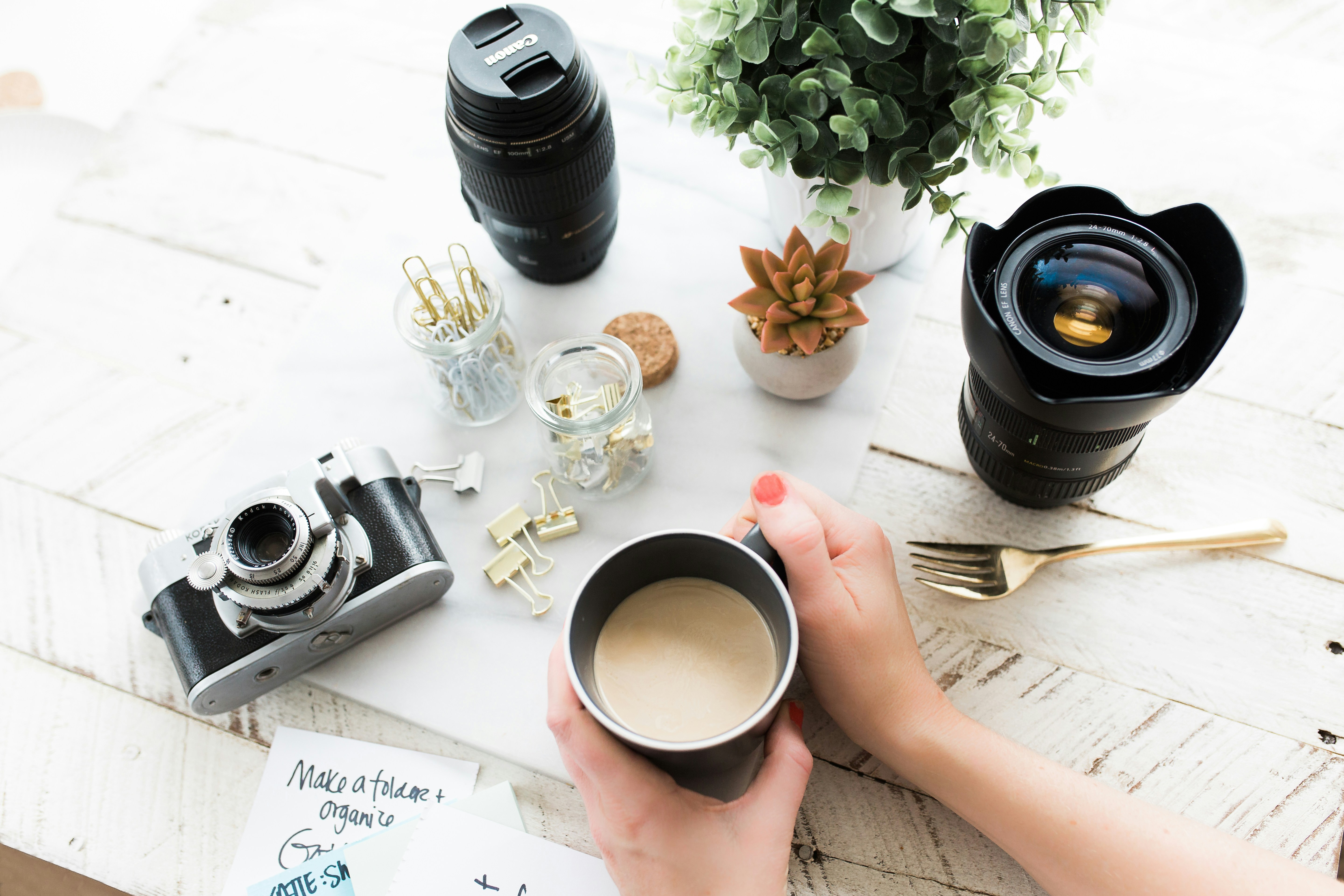 a camera, lenses and coffee laid out on a white desk