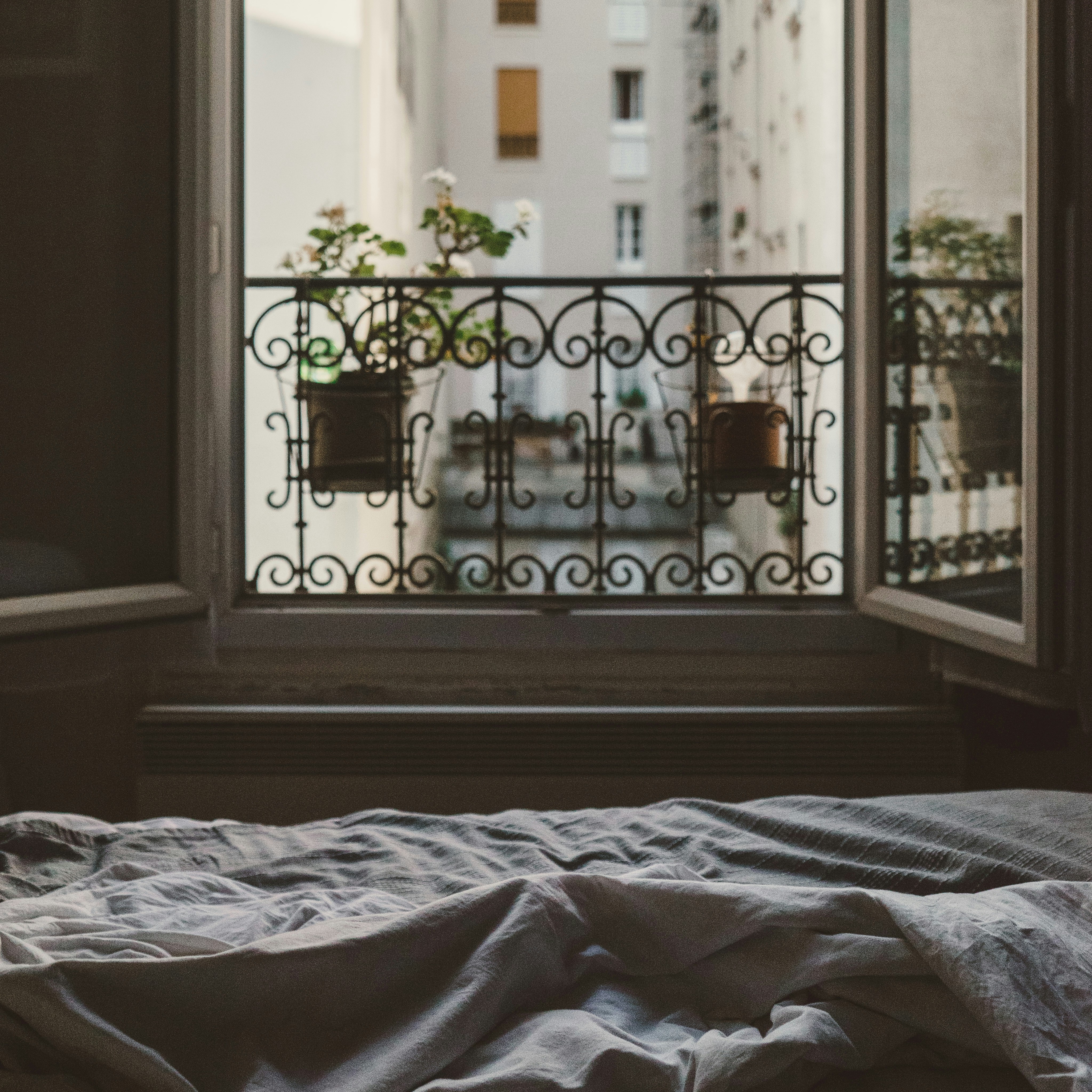 an unmade bed in a dim room with balcony doors beyond
