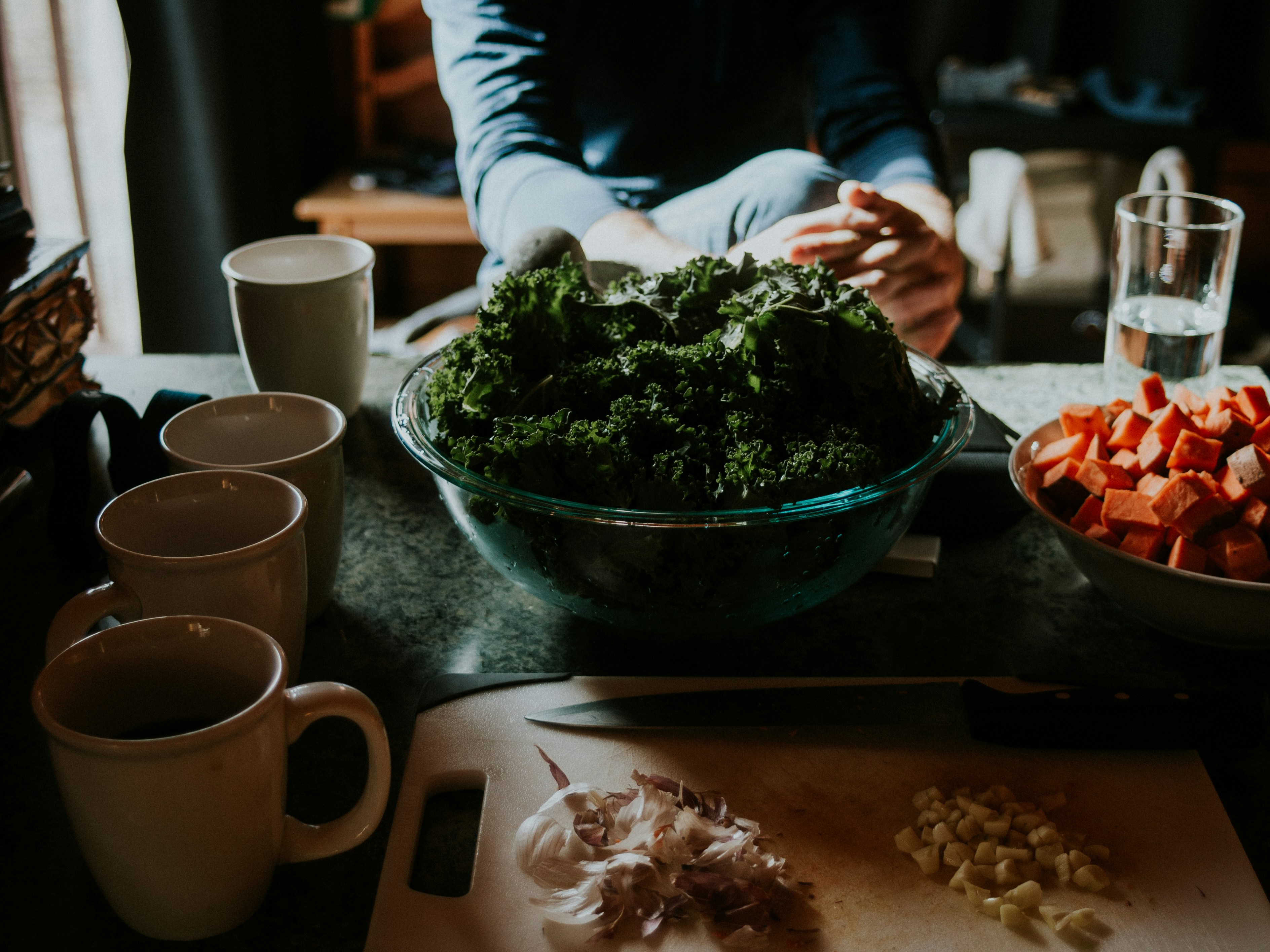 a kitchen counter mid-prep with greens and mugs