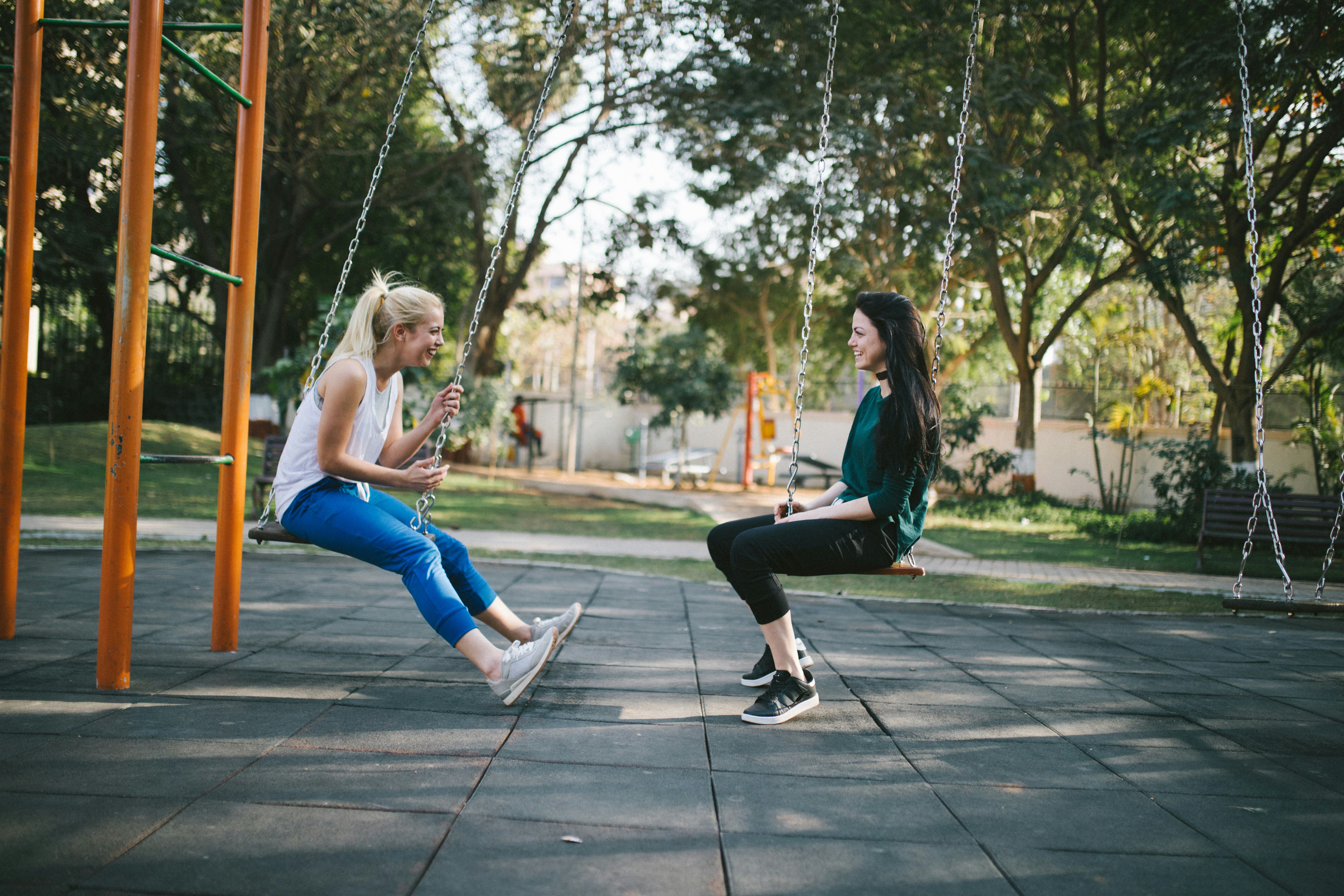 two women talking on swings in a park