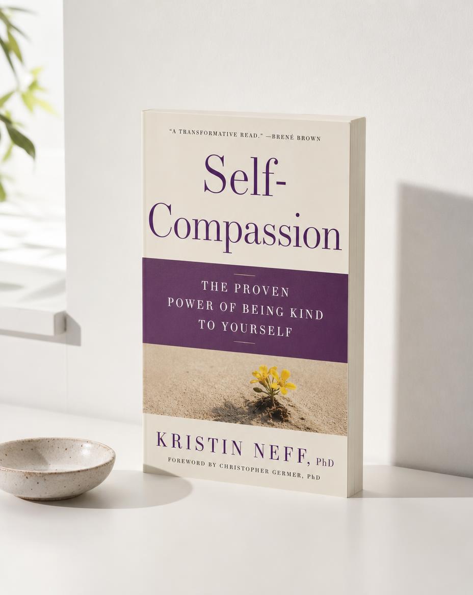 Self-Compassion by Kristin Neff standing on a white modern desk beside a small speckled dish.