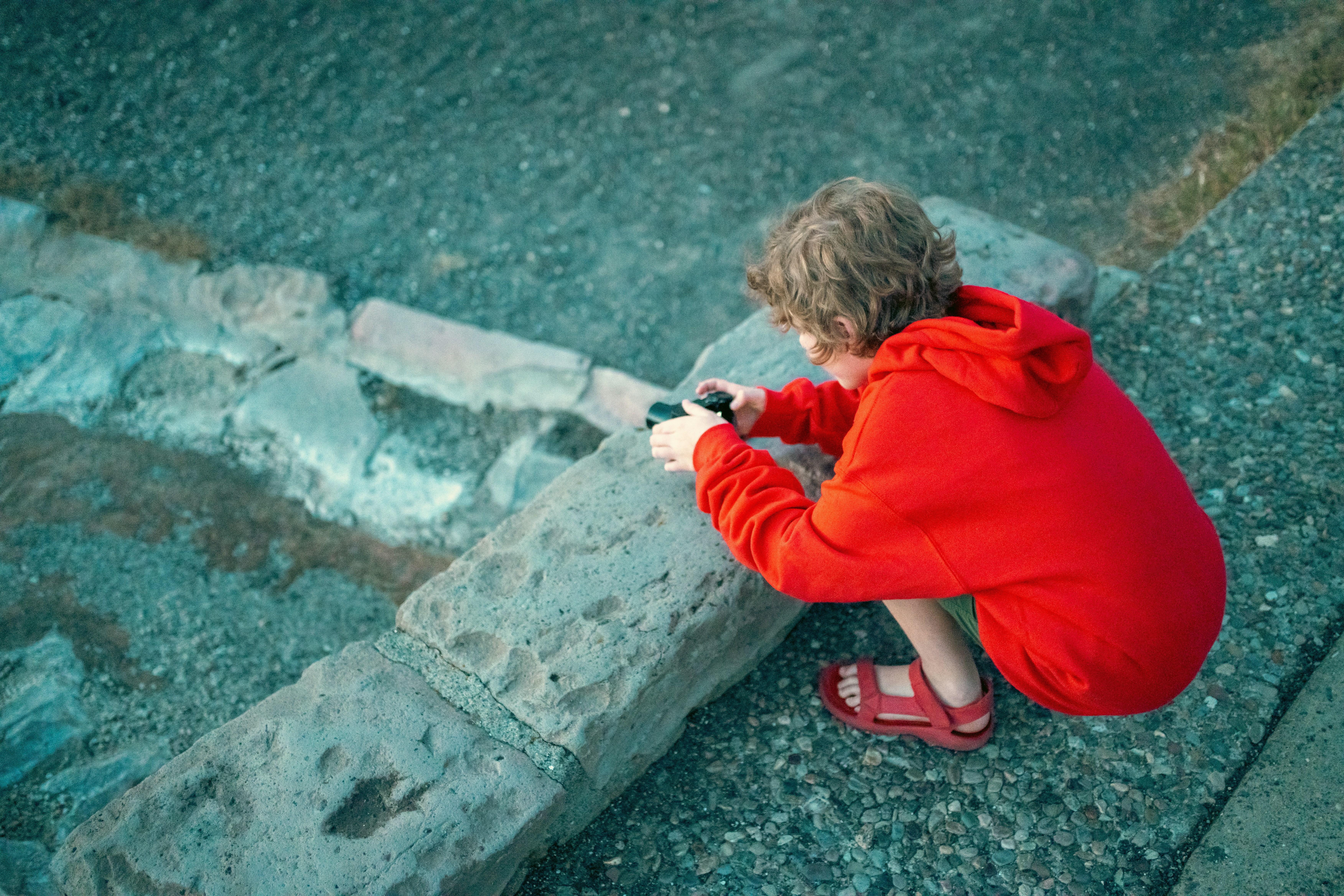 a child in a red coat crouched over chalk on the pavement
