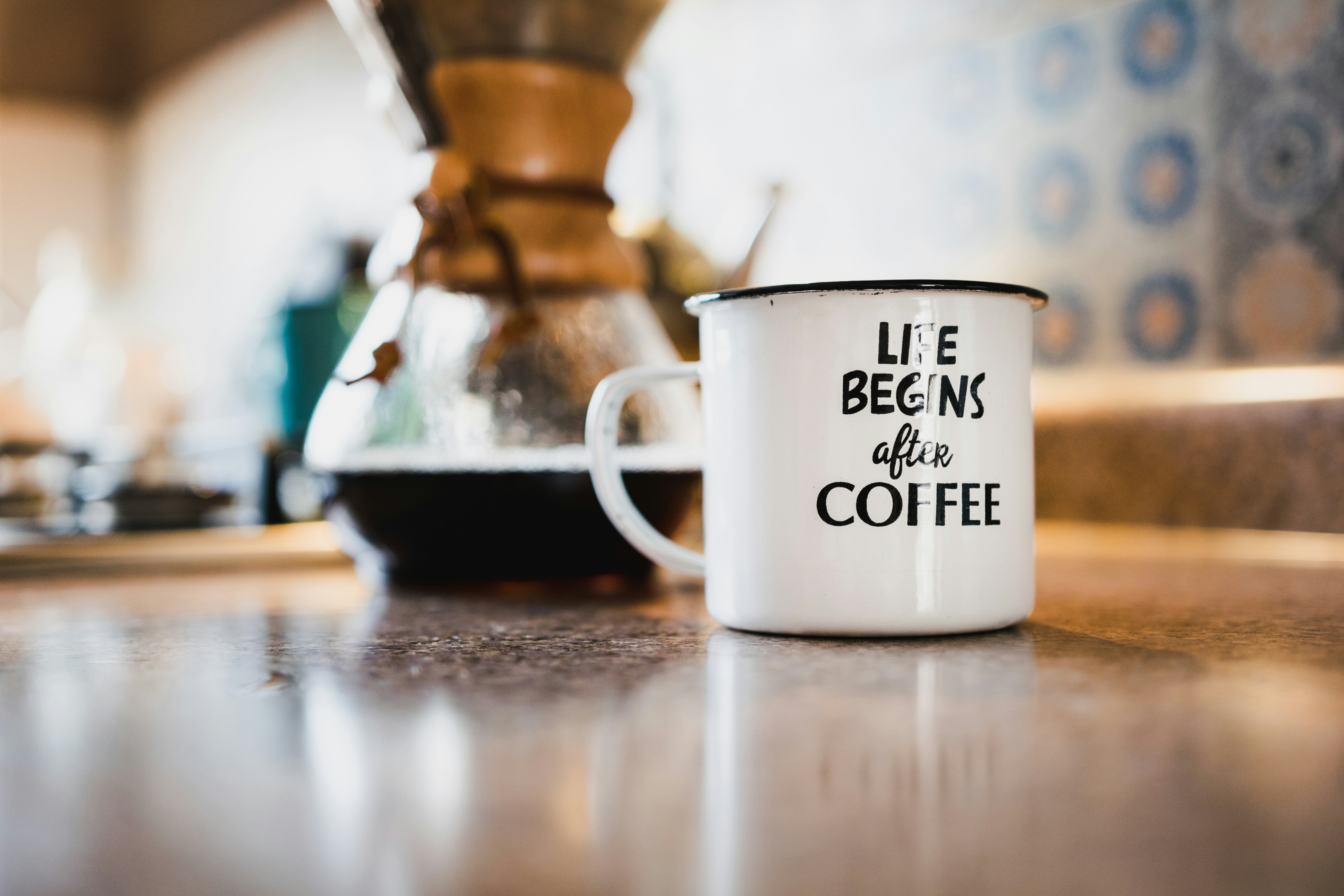 an enamel mug on a cafe counter reading life begins after coffee