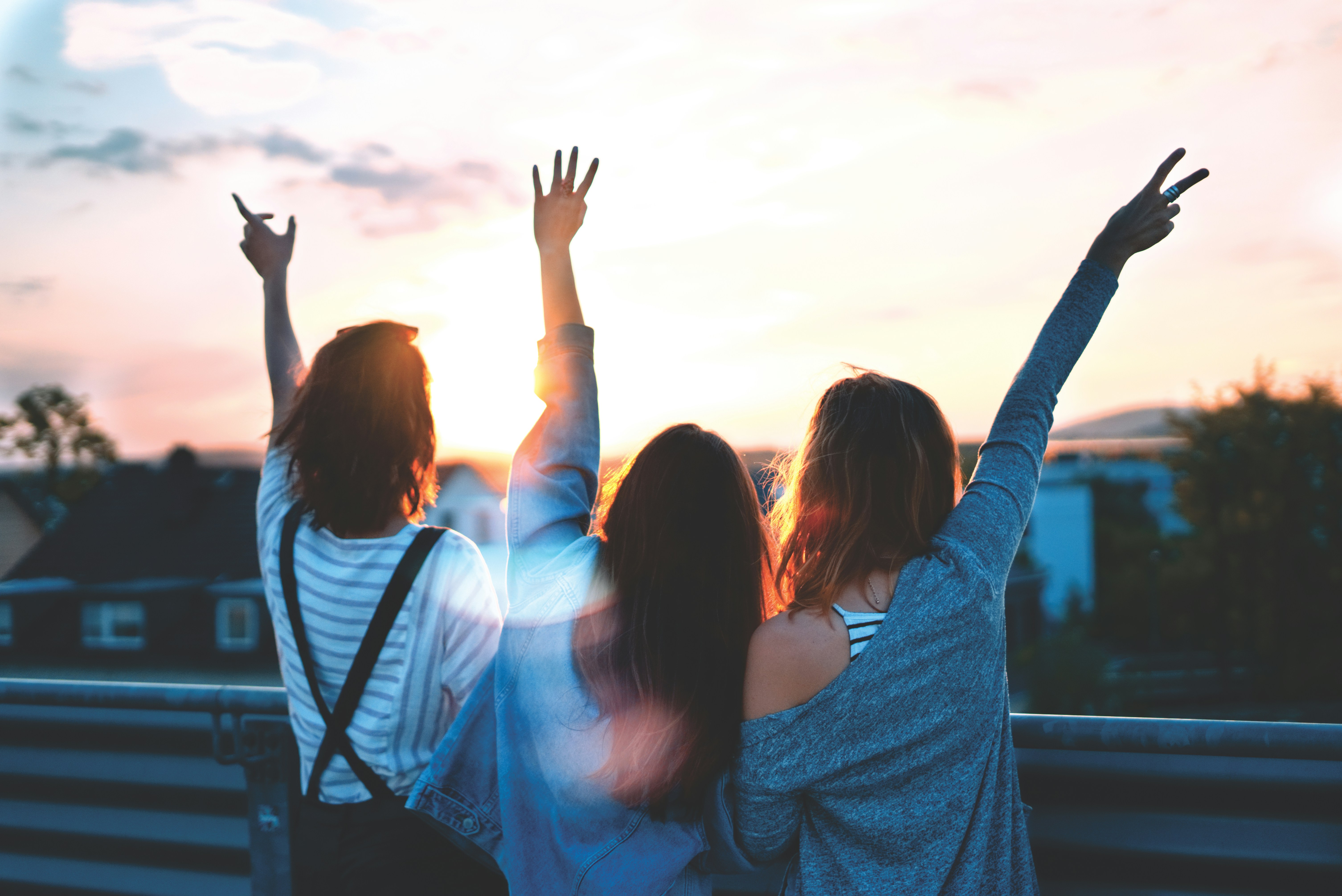 three friends with their arms raised against a sunset sky