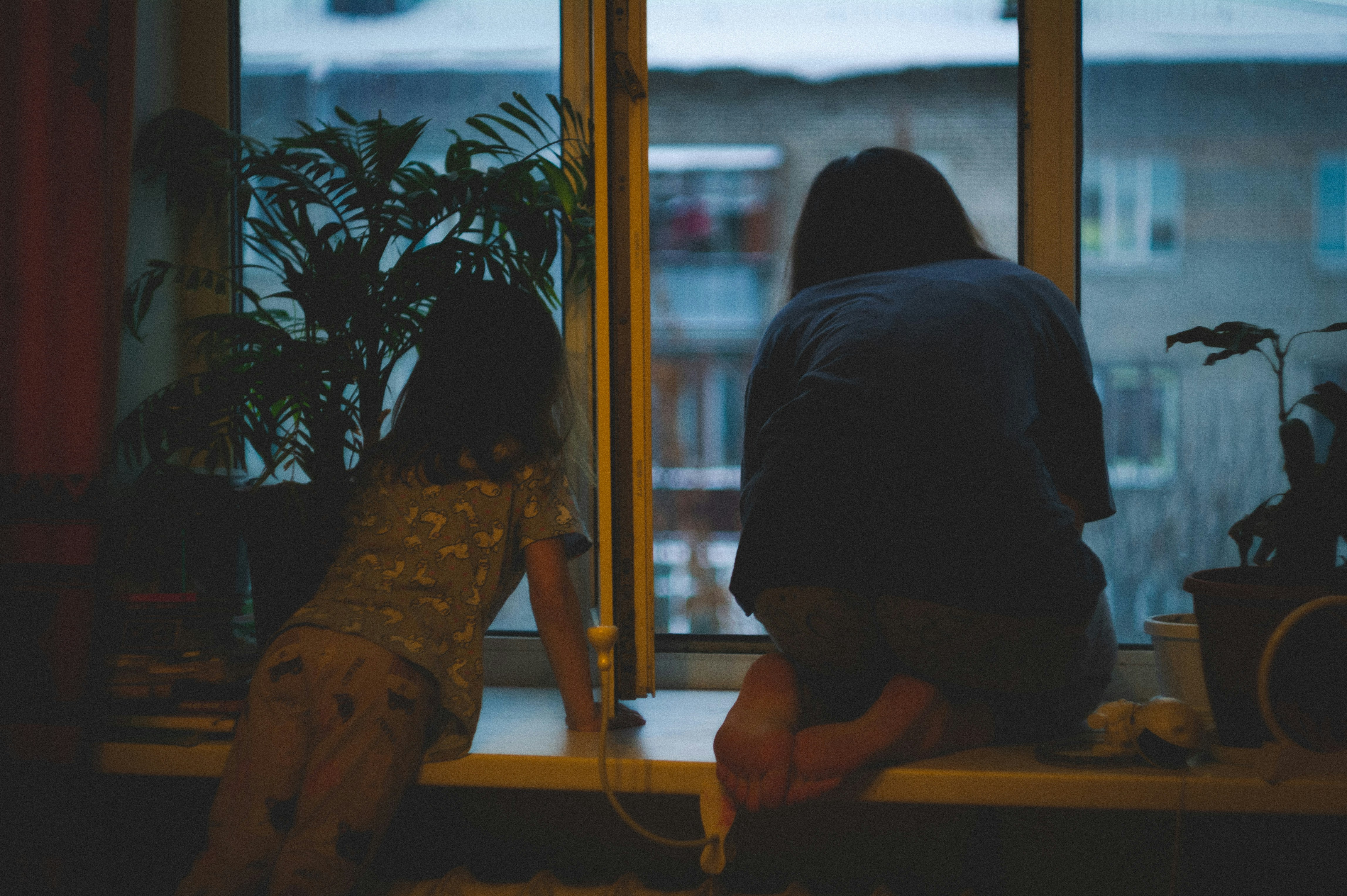 two people sitting on a windowsill looking out at dusk