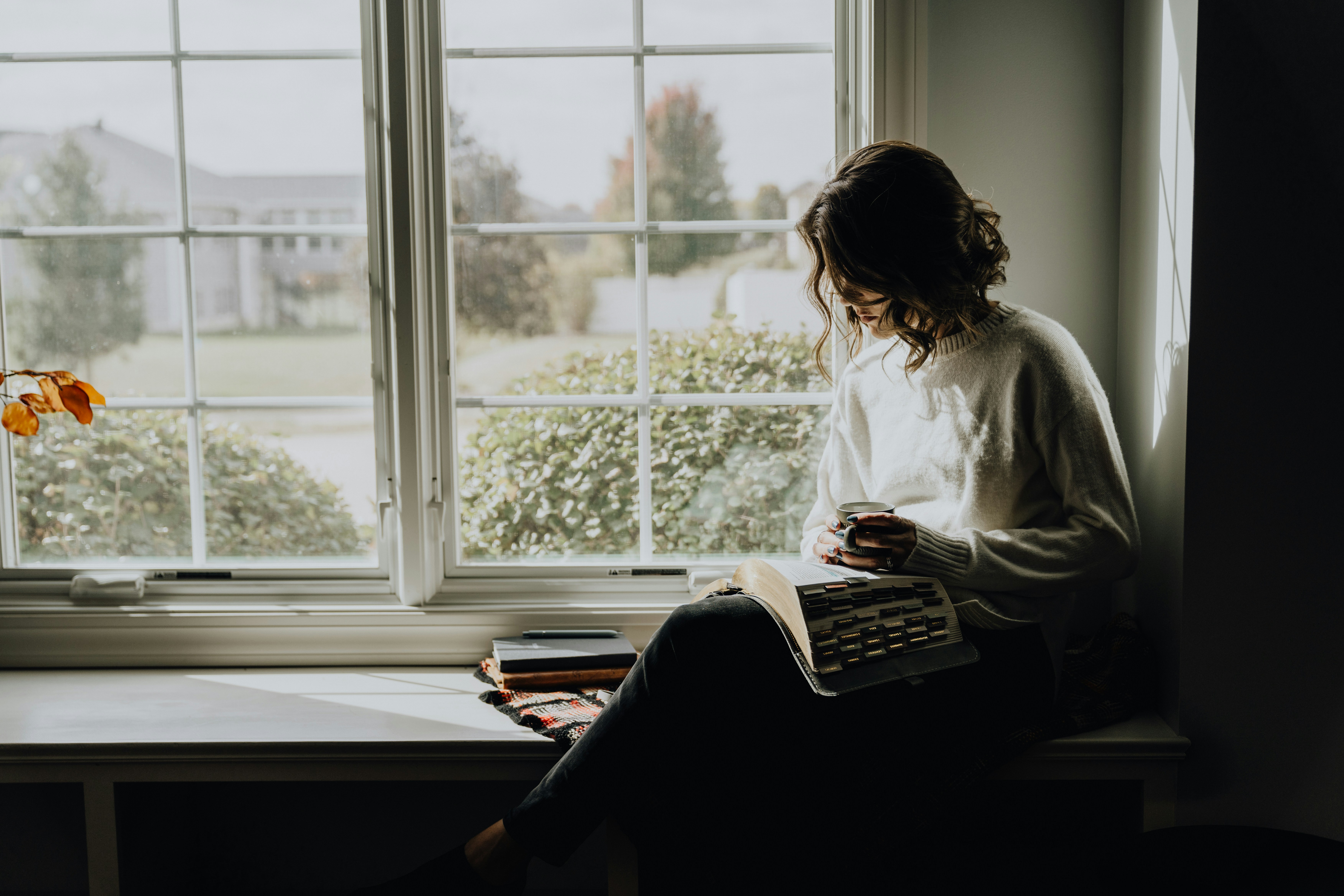a woman reading by a large window in a quiet room